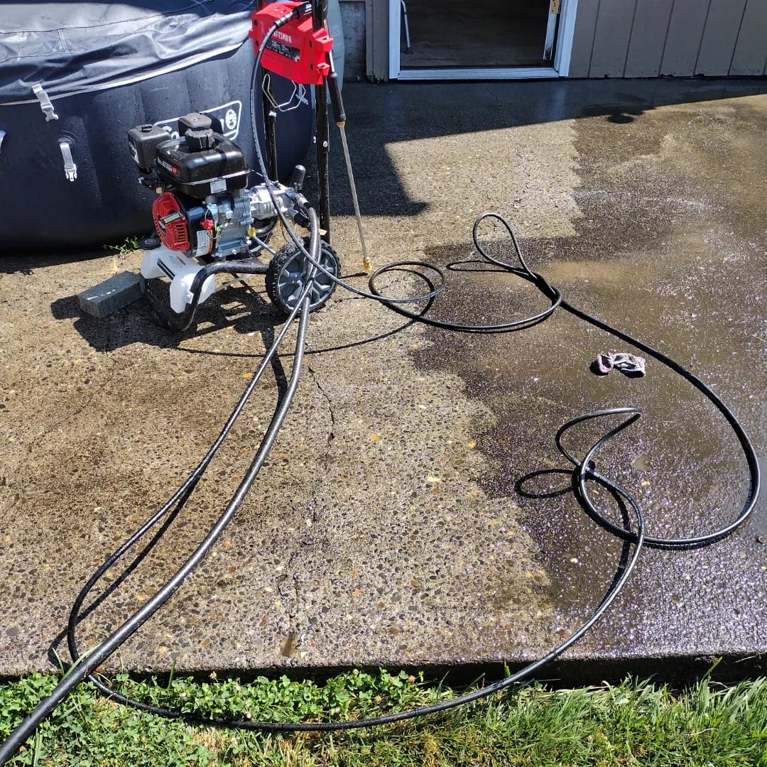 The Curb Appeal pressure washer and hoses set up on a wet patio, mid job